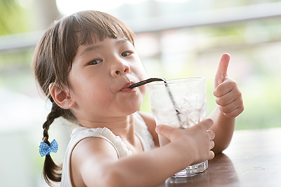 image of little girl drinking a glass of water from a straw giving a thumbs up
