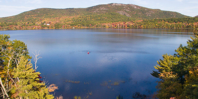 lake with trees surrounding it with a mountain in the background